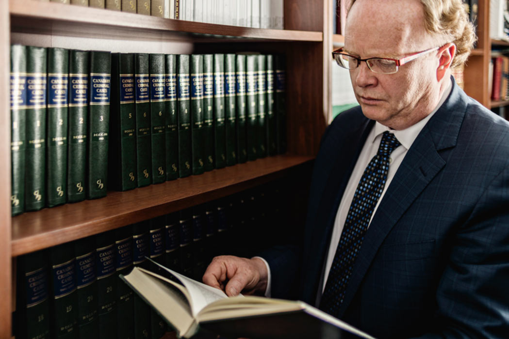 A defence lawyer, reading from a book in a law library